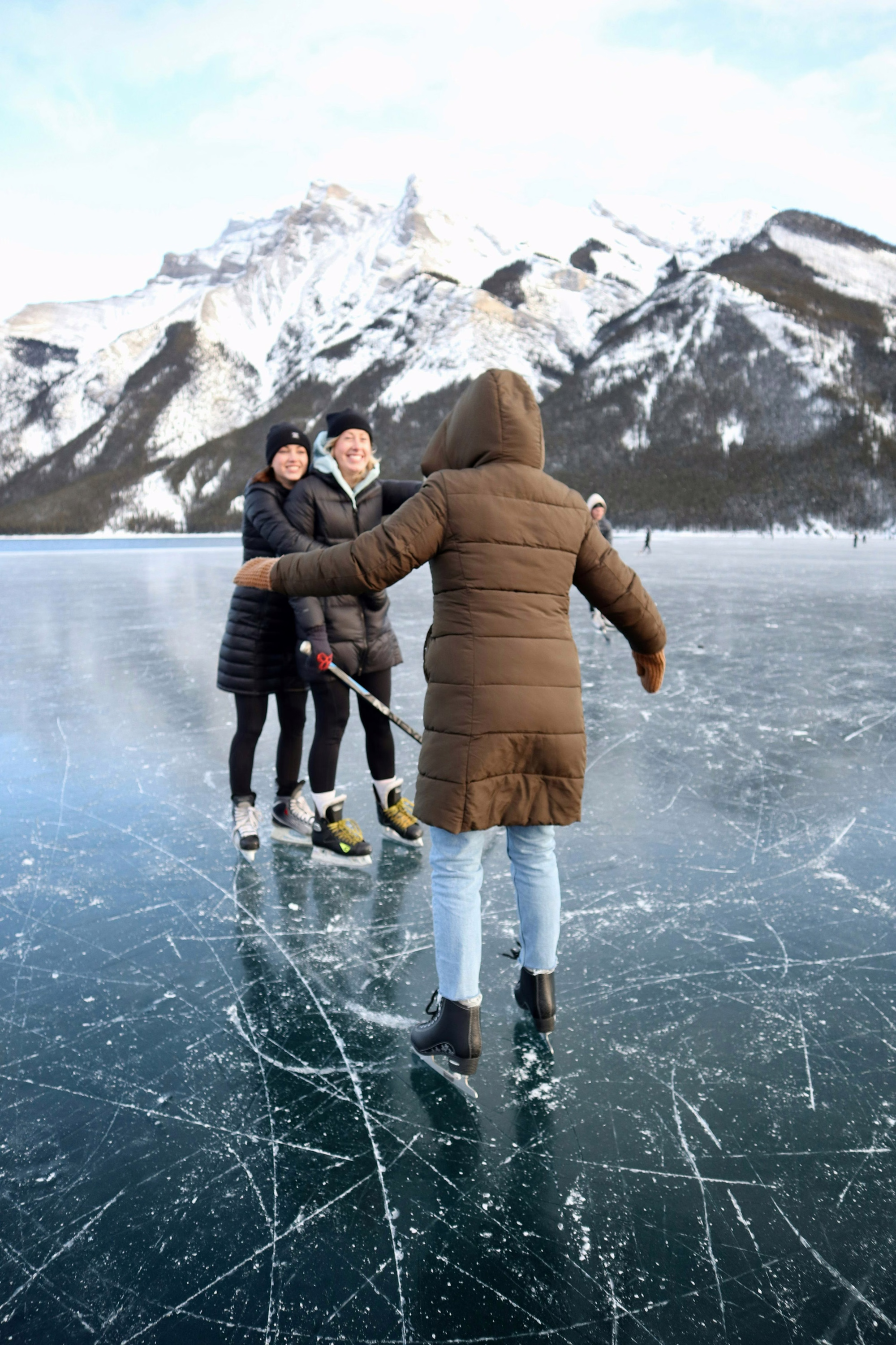 Skaters on an outdoor frozen lake beneath snowy mountains